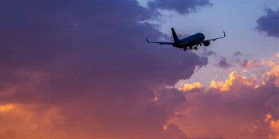 Silhouette of aircraft flying towards pink and purple clouds.