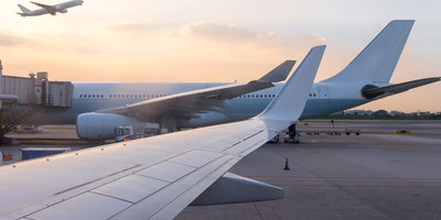 Two aircrafts at their terminals and another aircraft flying across the sky.